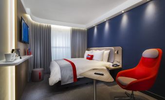 a hotel room with a red chair , gray bed , and blue walls , along with a desk and window at Holiday Inn Express Stockport