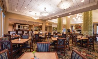 a large dining room with wooden tables and chairs , a bar area , and multiple chandeliers hanging from the ceiling at Hilton Garden Inn Meridian