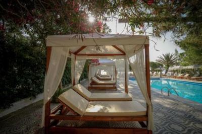 a canopy bed with white cushions is set up next to a pool and surrounded by trees at Hotel Summery