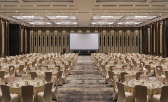 a large conference room with rows of tables and chairs , a projector screen at the front at Swissôtel Jakarta PIK Avenue