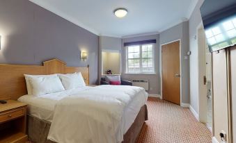 a large bed with white sheets and a wooden headboard is in the middle of a room with a window at Village Hotel Liverpool