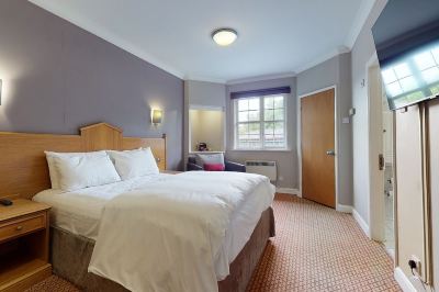 a large bed with white sheets and a wooden headboard is in the middle of a room with a window at Village Hotel Liverpool