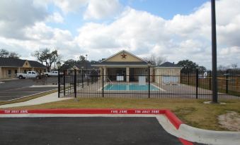 a house with a swimming pool and a fire station in front of it , under a blue sky with clouds at Hotel Texas Cuero