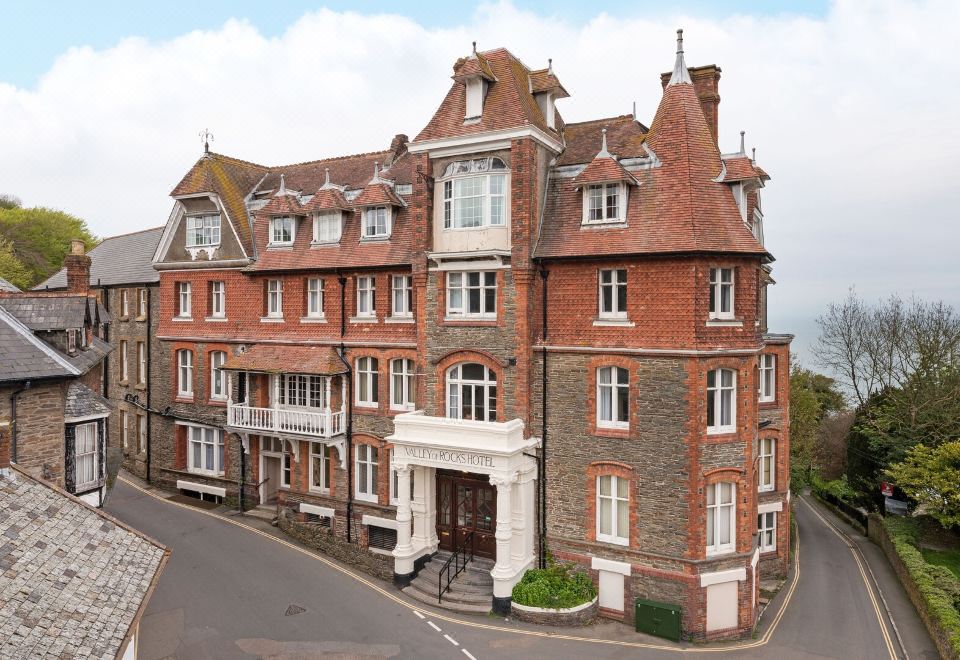 a large red brick building with a white porch and a balcony is shown in the image at The Valley of Rocks Hotel