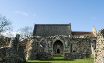 a stone building with an arched entrance is surrounded by green grass and trees under a clear blue sky at Brasteds