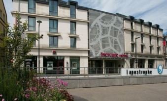 a modern hotel building with a large advertisement on its side , surrounded by flowers and trees at Mercure Chartres Cathedrale