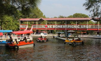 In front, there is a river with boats and people on the other side at Bombay Picnic Spot Hotel & Resort