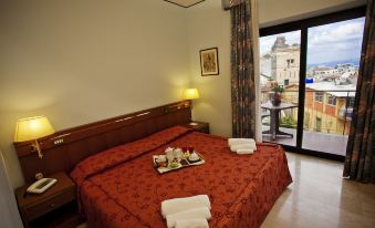 a hotel room with a red bedspread , white towels , and a window with a view of the city at Augustus