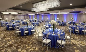 a large banquet hall with numerous tables and chairs , some of which are covered in blue tablecloths at San Mateo Marriott San Francisco Airport