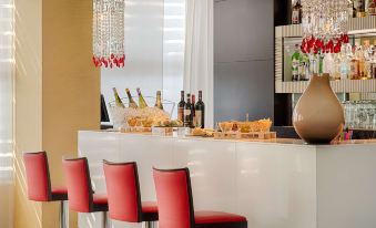 a dining area with a white bar counter , red chairs , and a variety of food and drinks at Savhotel Mantegna Padova