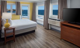 a hotel room with a bed , television , and floor - to - ceiling windows overlooking the ocean at Ashworth by the Sea