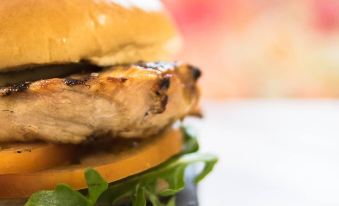 a close - up image of a chicken sandwich on a bun with lettuce and tomato on a black plate at 42 Apart-Hotel