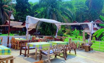 an outdoor dining area with wooden tables , chairs , and umbrellas , surrounded by lush greenery and mountains at Holiday Resort