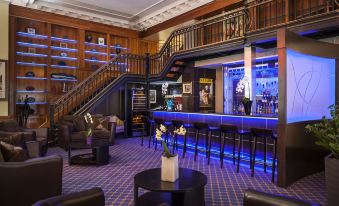 a modern bar with a wooden ceiling , blue lights , and a central counter , along with several chairs and tables at LHotel