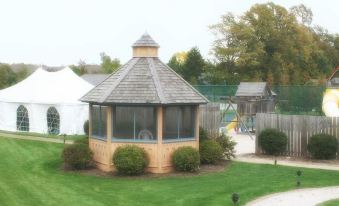 a wooden gazebo with a stone roof is surrounded by green grass and trees , with a playground in the background at Scandinavian Lodge