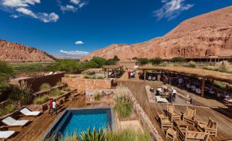 a large outdoor pool area with wooden tables and chairs , surrounded by mountains and greenery at Nayara Alto Atacama