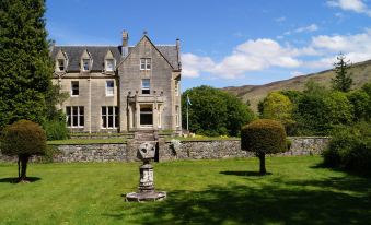 a large stone house with a statue in the front yard , surrounded by grass and trees at Glengarry Castle Hotel