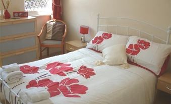 a well - decorated bedroom with a white bed , red and white floral bedspread , white comforter , pillows , and a small table with at The Royal Oak