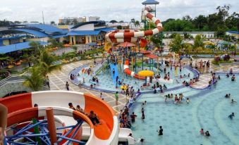 a large water park with numerous people enjoying various water slides , pools , and attractions , as well as a building in the background at Pematang Siantar