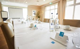 a long table with white tablecloths and water bottles , glasses , and a water carton , set up for a meeting in a conference at Trearddur Bay Hotel