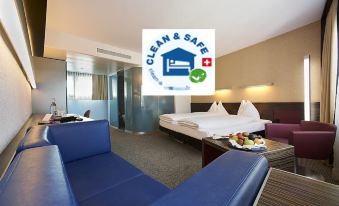 a clean and safe hotel room with a blue couch , bed , and a dining table at Hotel Ambassador
