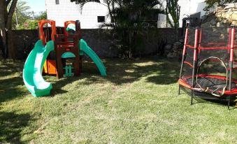 a backyard with a swing set , slide , and trampoline , surrounded by green grass and trees at Hotel du Lac Macae