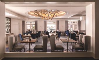 a modern dining room with multiple tables and chairs , a large chandelier , and windows at The Ritz-Carlton, Marina del Rey