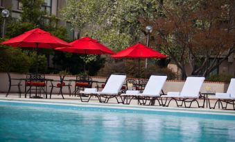 a swimming pool with white lounge chairs and red umbrellas , set against the backdrop of a building at Washington Dulles Airport Marriott