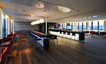 a modern bar with black and white furniture , including a long bar with stools and hanging lights at Quality Hotel Fredrikstad