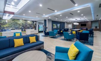 a large , well - lit room with blue and yellow seating and a mural on the wall at La Quinta Inn & Suites by Wyndham Tifton