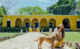 a woman and her dog are standing in front of a yellow building with an archway , posing for a picture at Hacienda San Miguel Yucatan