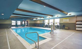 a large indoor swimming pool with a blue ceiling and white walls , surrounded by chairs and tables at Home2 Suites by Hilton Springdale Cincinnati