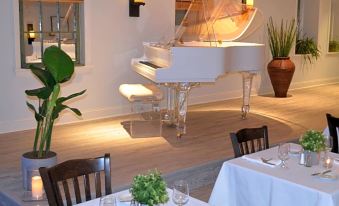 a dining room with two white tables and chairs , a piano in the background , and potted plants on either side at Southampton Inn