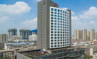 a tall building with a red logo on top is surrounded by other buildings and has a blue sky in the background at M Hotel