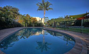 a large , empty swimming pool surrounded by trees and a building in the background , with a clear blue sky above at Quality Hotel Robertson Gardens