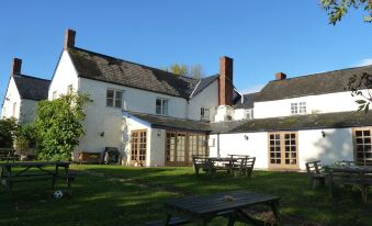 a large white house surrounded by a grassy field , with several picnic tables and benches outside at The Carew Arms