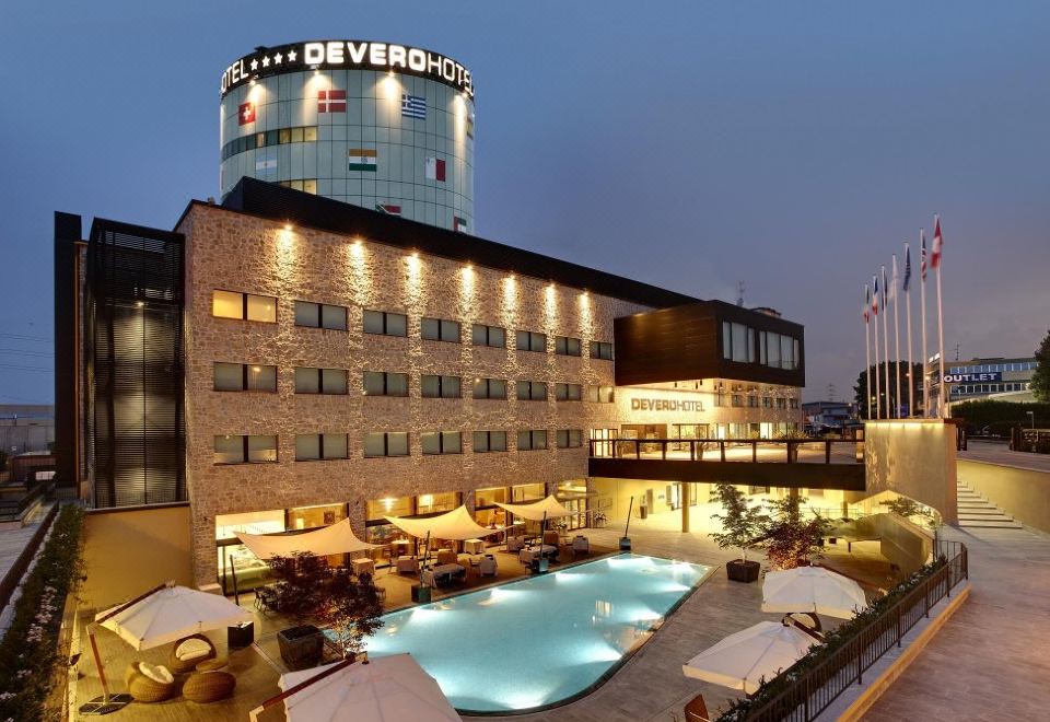 a large hotel with a swimming pool surrounded by chairs and umbrellas , located in a city at Devero Hotel  Spa, BW Signature Collection