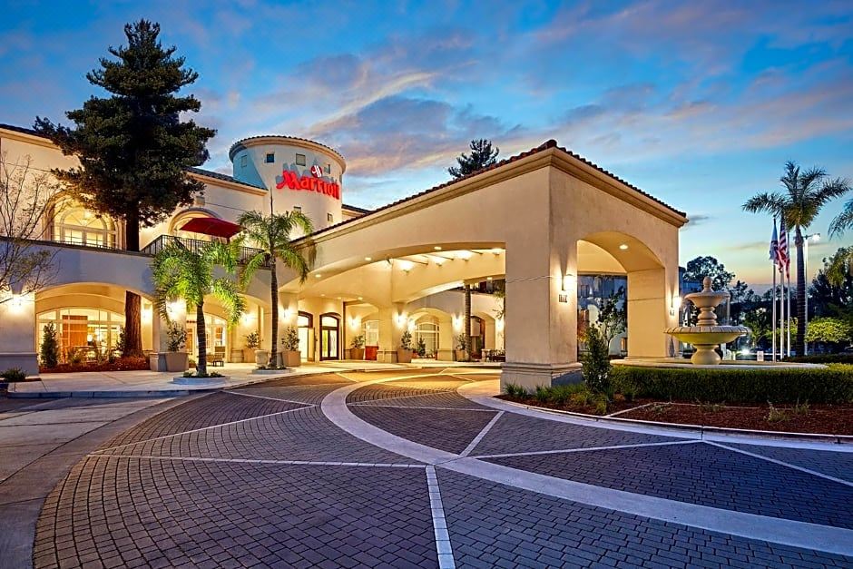 a hotel entrance with a red and white checkered floor , surrounded by palm trees , under a clear blue sky at San Mateo Marriott San Francisco Airport