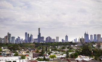 a city skyline with a mix of residential and commercial buildings , surrounded by trees and houses at The Cullen Melbourne - Art Series