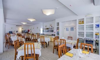 a large dining room with wooden chairs and tables , white tablecloths , and a kitchen in the background at Hotel New York