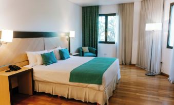 a large bed with a green blanket and white pillows is in a room with wooden floors and a window at Hotel Plaza Central Canning