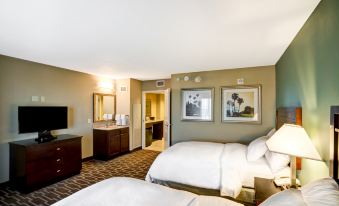 a hotel room with two beds , a bathroom , and a desk , all decorated in neutral colors at Embassy Suites by Hilton Fort Myers Estero