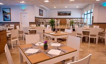 a modern restaurant with white tables and chairs , wooden tables , and large windows , ready for dining at Hotel Loar Ferreries