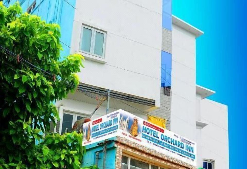 "a white building with a blue sign that says "" hotel kerensa hotel "" in front of trees" at Hotel Orchard Inn