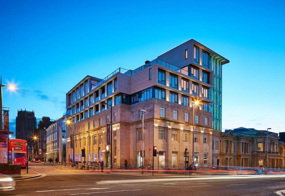 a large building with a red brick facade is located on a street corner at dusk at Hope Street Hotel