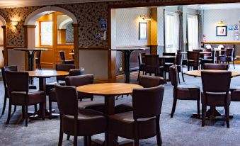 a dining room with several tables and chairs , some of which are occupied by people at Cairn Hotel