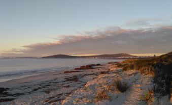 a sandy beach at sunset , with the sun setting over the ocean and clouds in the sky at Emu Point Motel