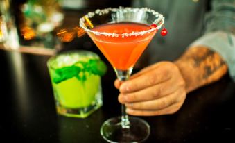 a bartender holding a red cocktail in a martini glass , with a green drink nearby at Radisson Blu Hotel Uppsala
