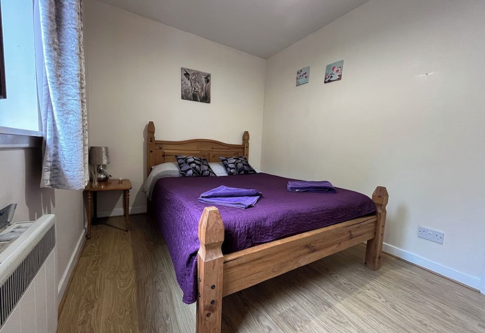 a cozy bedroom with a wooden bed , a purple comforter , and a vase on the nightstand at River View Apartment