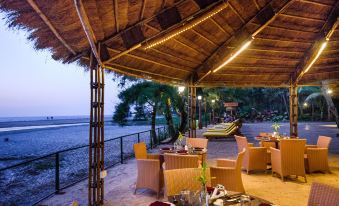 a restaurant patio with wooden tables and chairs , overlooking a body of water during sunset at Beleza by the Beach